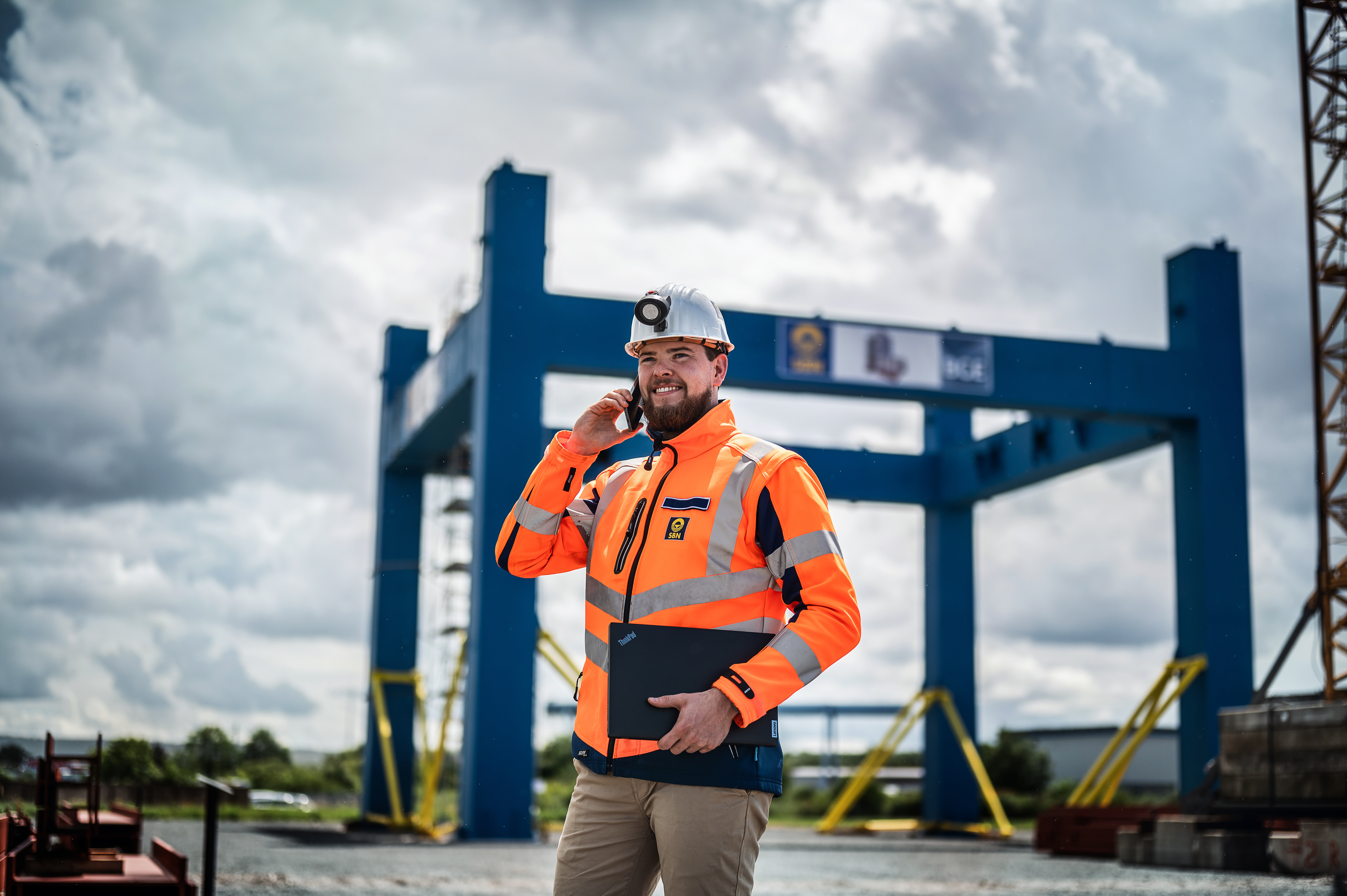 Ein Student in Arbeitskleidung telefoniert auf einer Baustelle