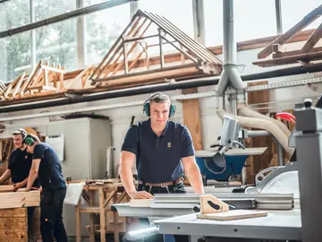  Zimmerer bearbeiten Holz mit Nagelschussgeräten, Bohrmaschine sowie Säge und Hobel.